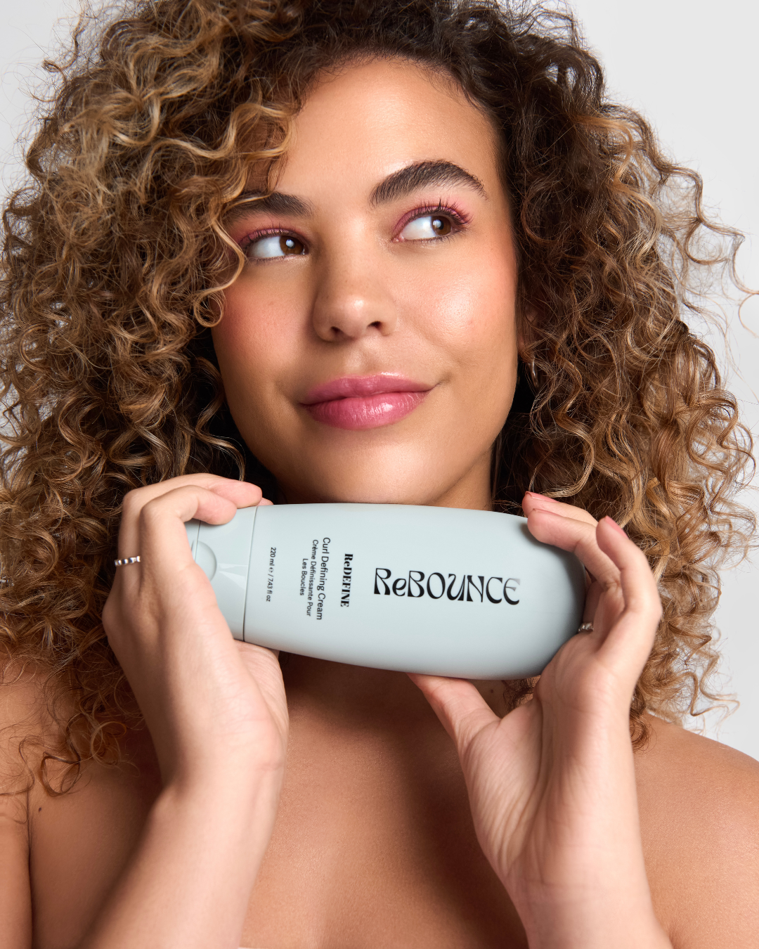 Woman holding a ReBounce curl defining cream product against a neutral background